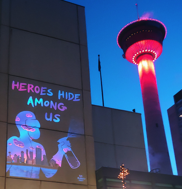 The Calgary tower beside a projection of artwork depicting a Calgary city scape inside the silhouette of a cleaner with the title Heroes Hide Among Us
